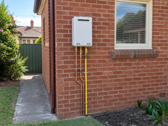Wall-mounted hot water unit with copper and gas lines on a brick house exterior in Bexley